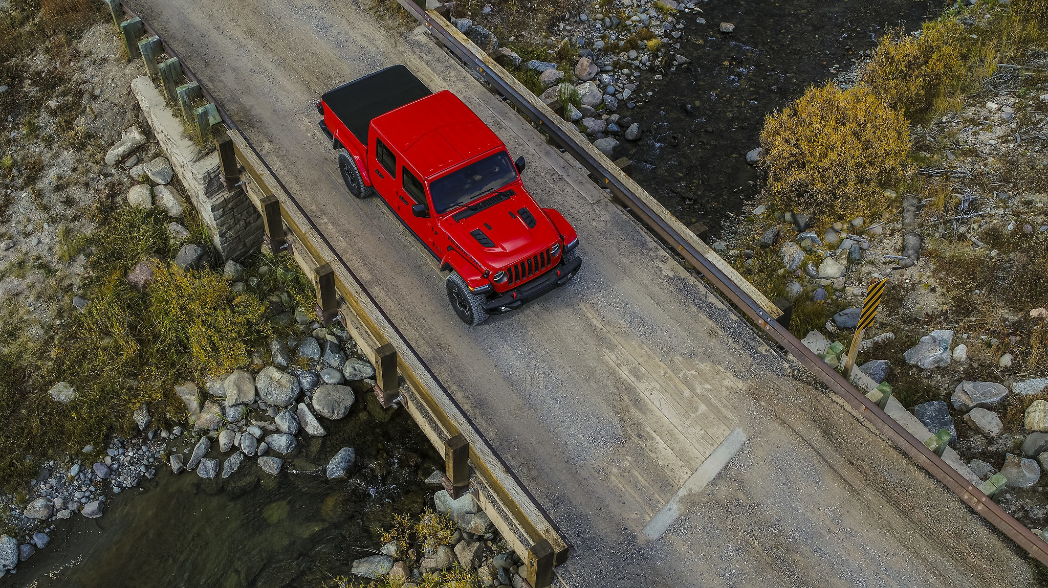 Vue du ciel d'un Jeep Gladiator Rubicon 2021 garé sur un pont de bois d'un chemin de terre au-dessus d'un ruisseau