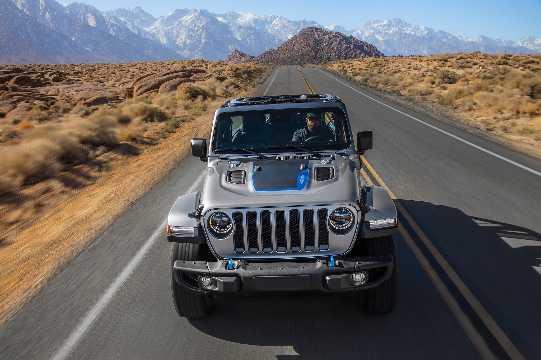 A man driving a topless 2021 Jeep Wrangler 4xe on a road with mountains in the background