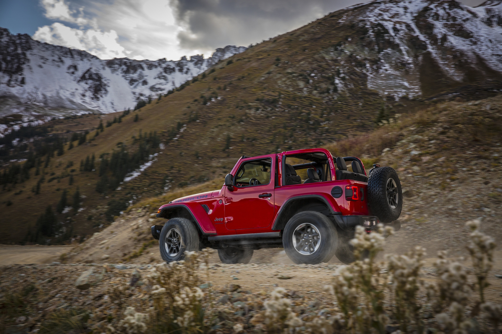 A top-less 2021 Jeep Wrangler Rubicon driving down a dirt road at the bottom of snowy mountains