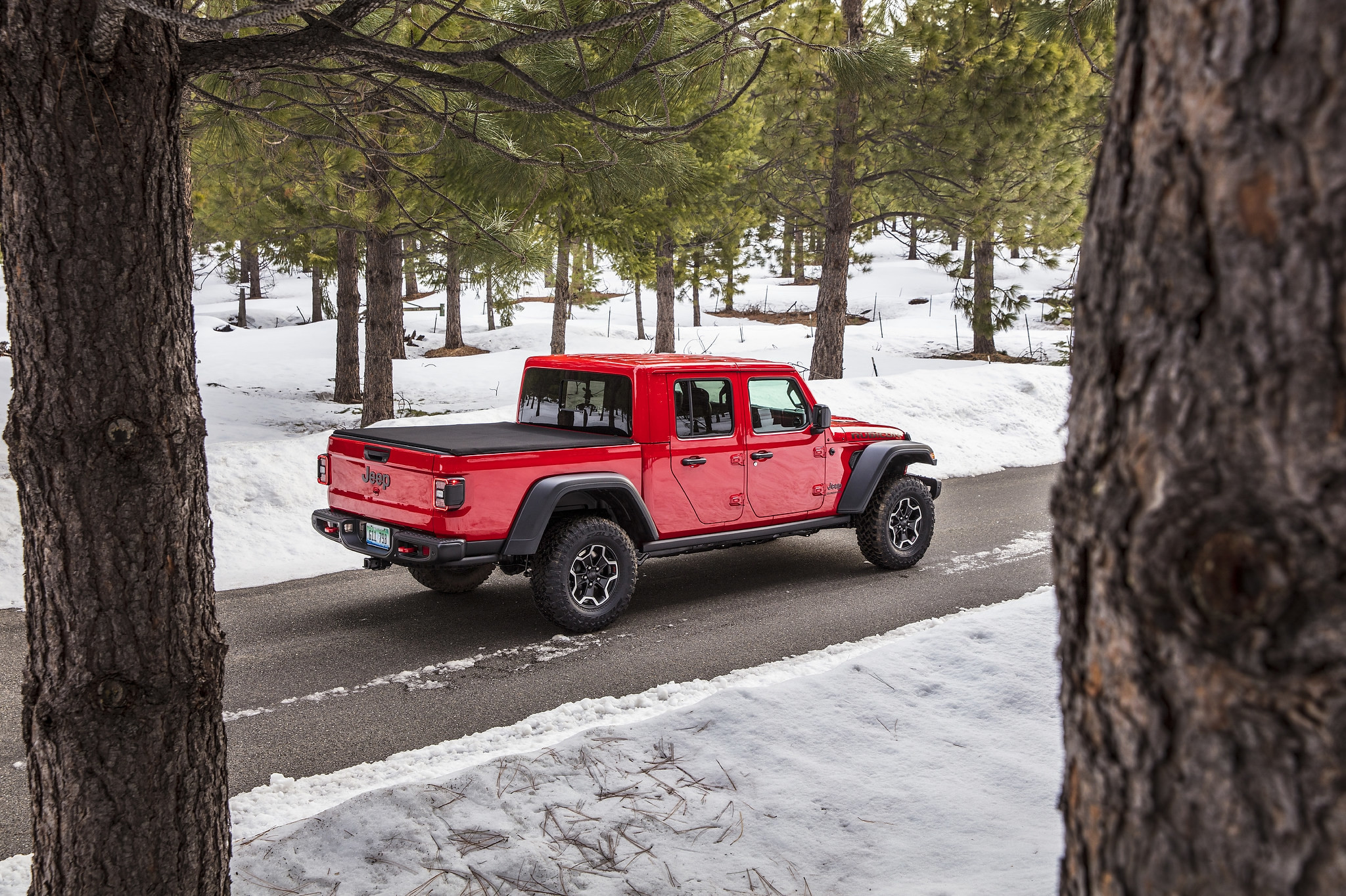 A 2021 Jeep Gladiator Rubicon parked on a road surrounded by a snow-covered forest