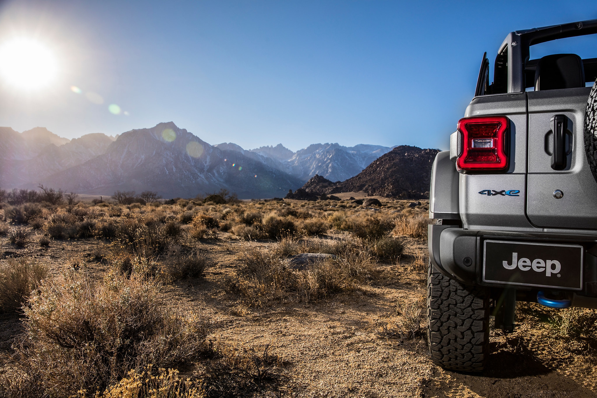 À gauche, vue d’un paysage désertique avec des montagnes au loin et surplombé par un soleil brillant, et à droite, vue arrière du Jeep Wrangler 4xe 2021 côté conducteur