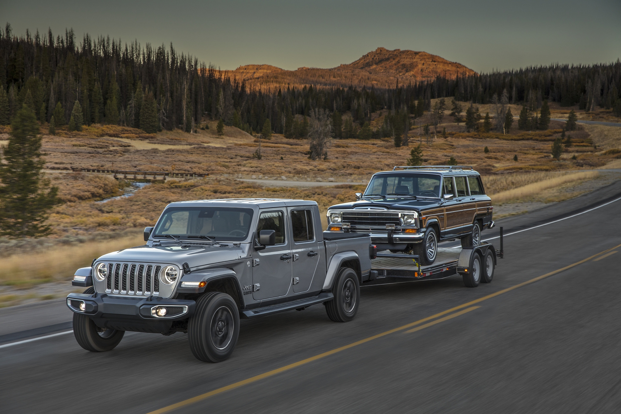Un Jeep Gladiator Overland 2021, tirant une remorque transportant un véhicule, circule sur une route de campagne