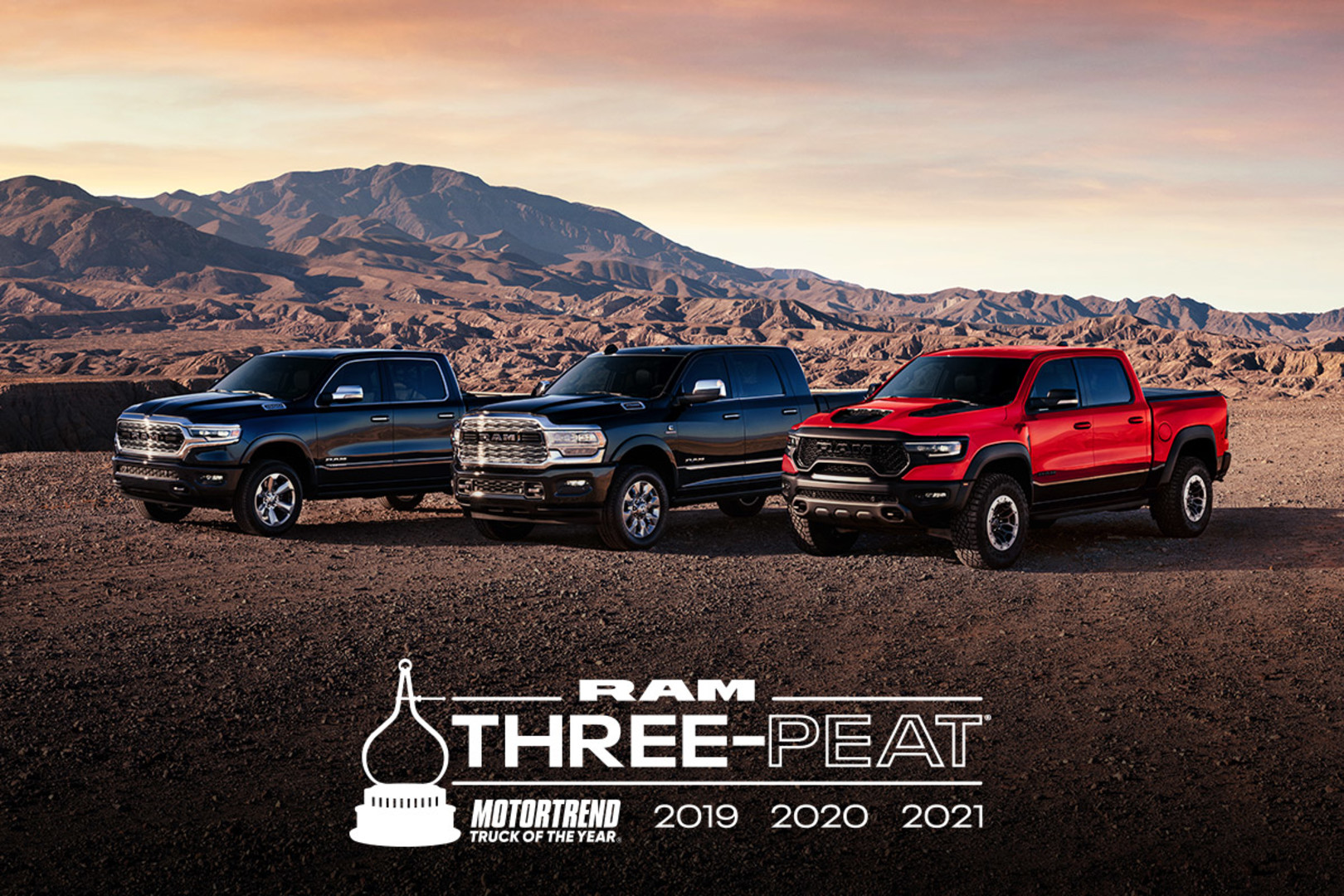 Lineup of three Ram trucks in a rocky desert surrounded by a mountain range. Ram Three-Peat MotorTrend Truck of the Year 2019 2020 2021.