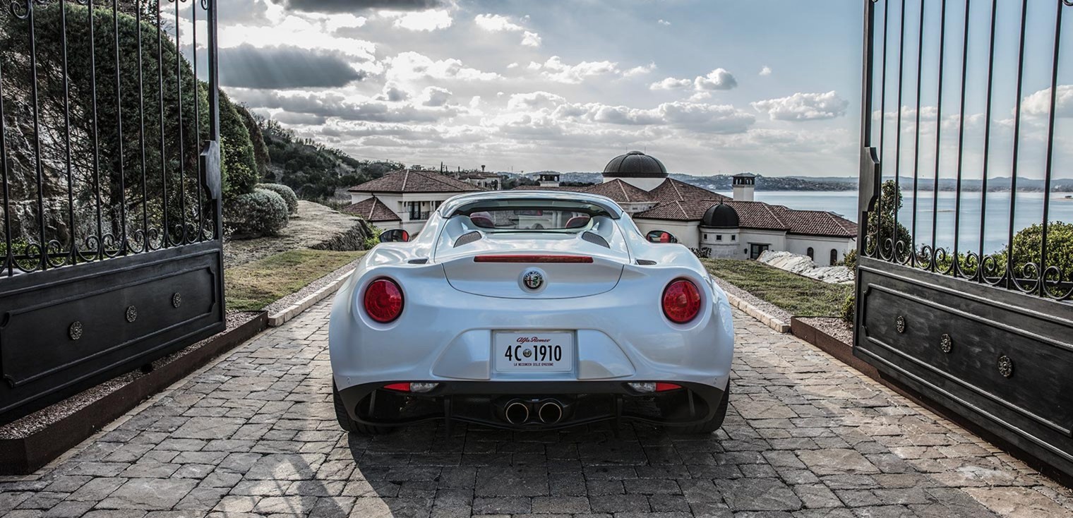 Vue arrière de l’Alfa Romeo 4C Spider 2019, illustrée en blanc, sortant d’une allée clôturée