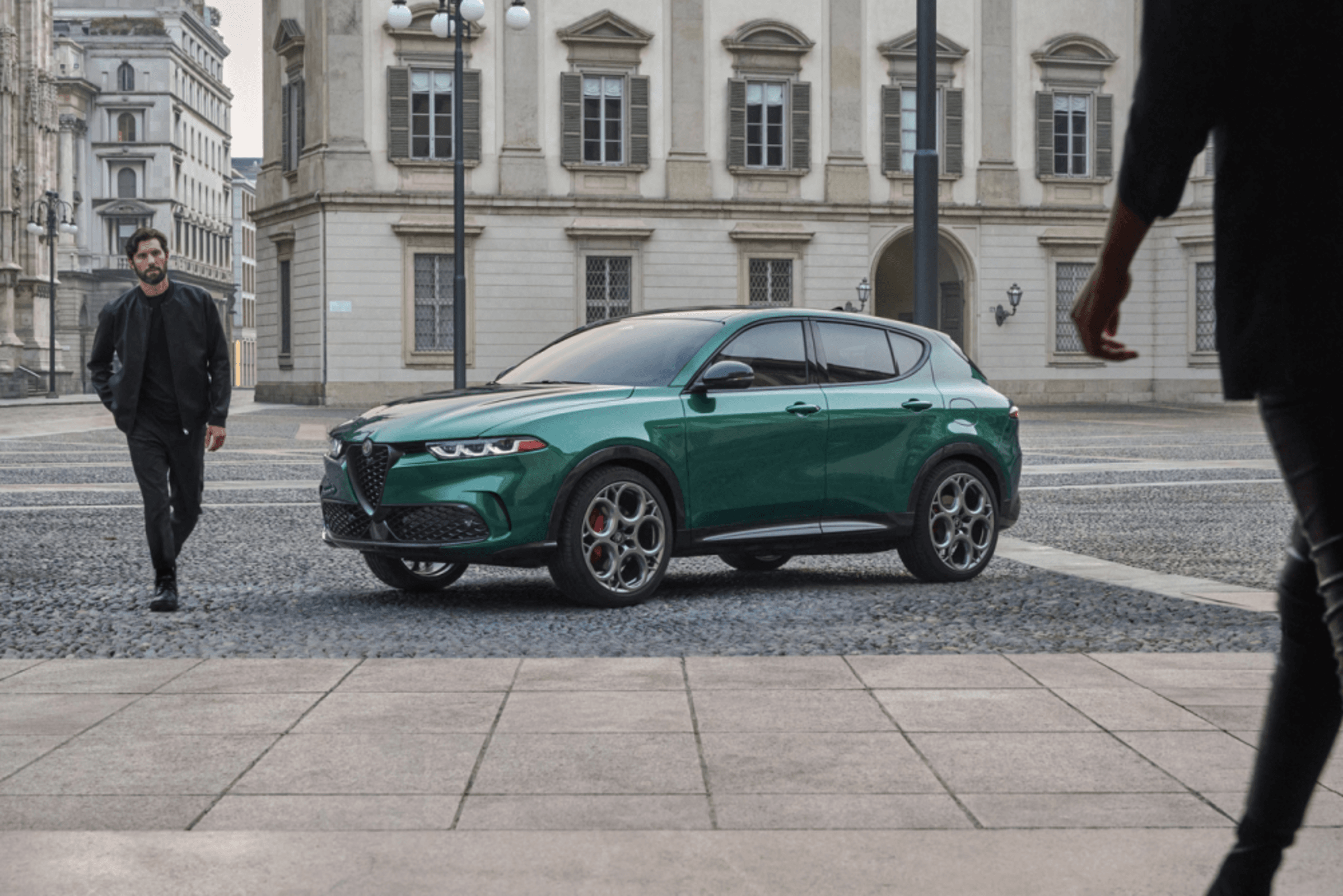 Vue de profil d'une Alfa Romeo VHR 2023 verte garée à l'extérieur d'un bâtiment avec un homme marchant devant le véhicule.