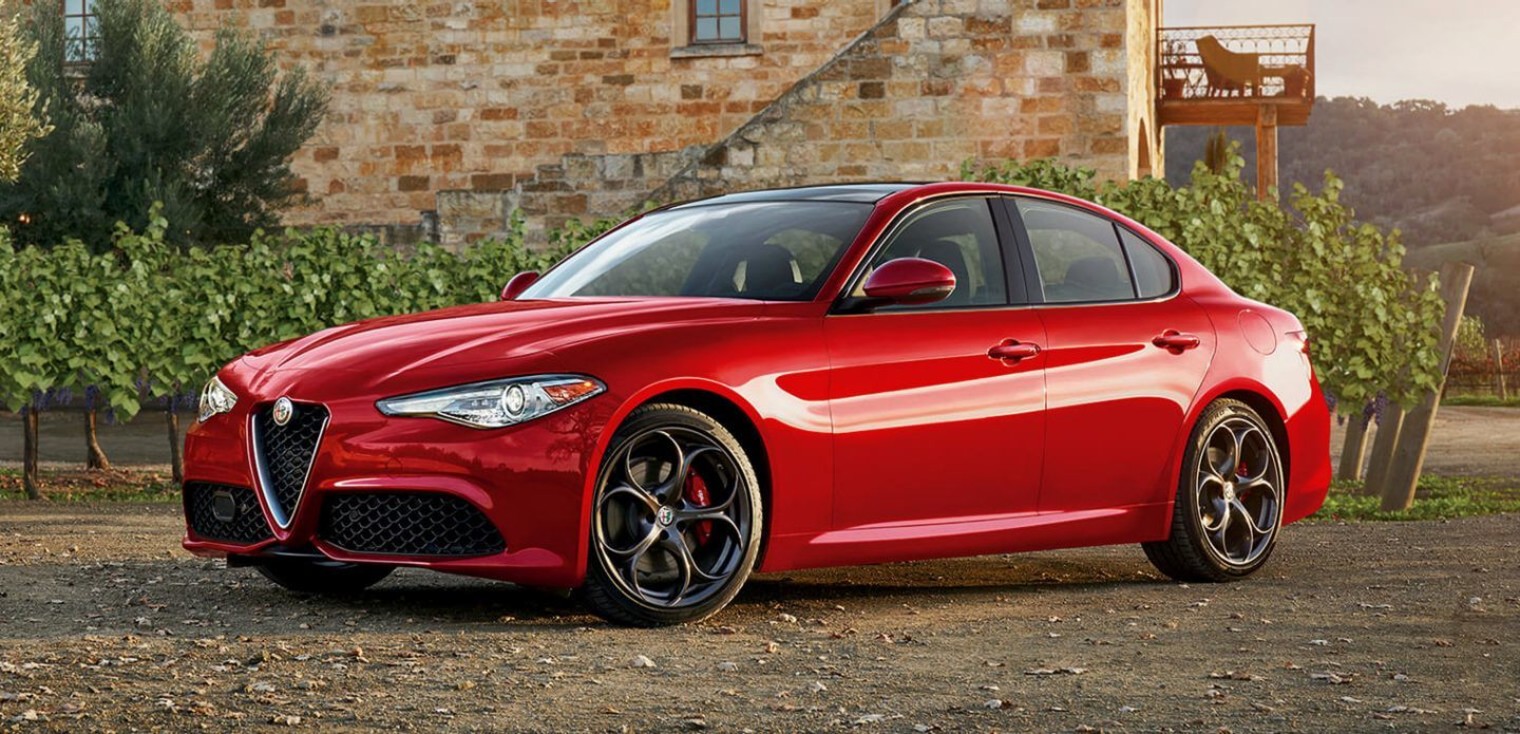 Front view of the red 2019 Alfa Romeo Giulia parked on an open field with a building in the background