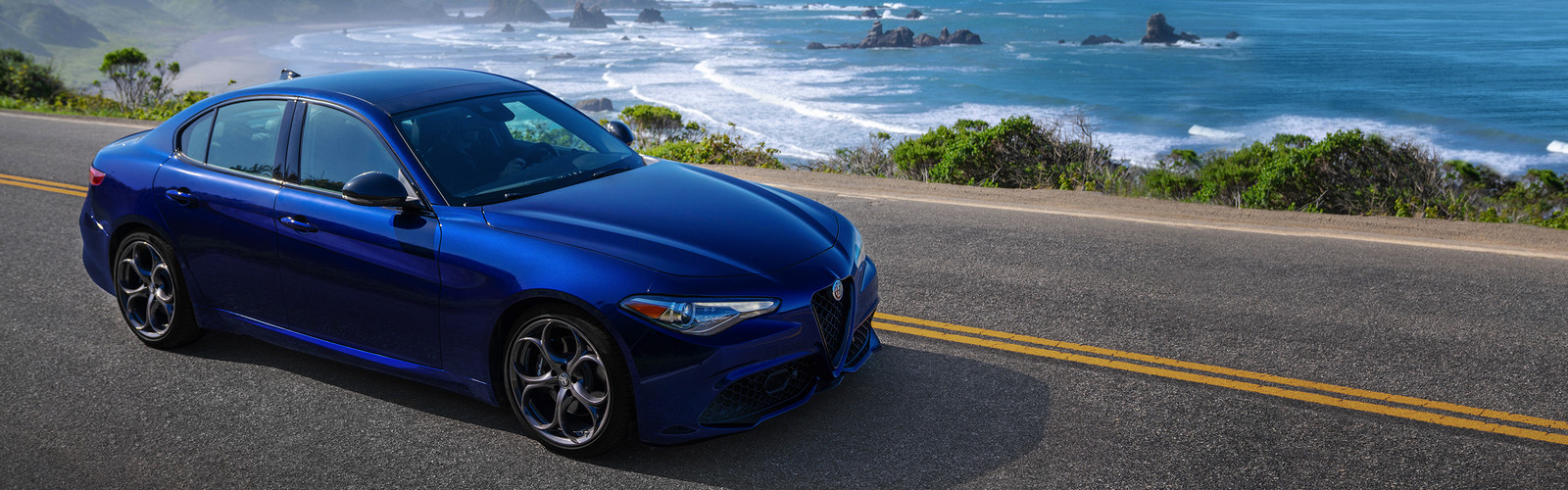 Une Alfa Romeo Giulia 2019 bleue roulant sur une route pavée le long de la côte.