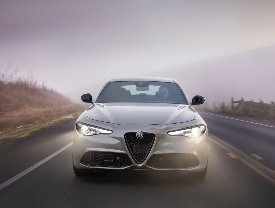 A front view of the 2020 Alfa Romeo Giulia on the road with its headlamps on.