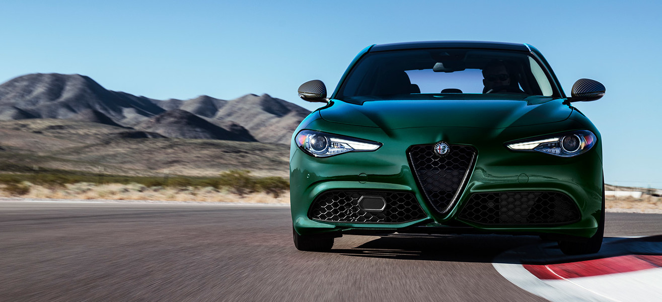 Front view of a green 2021 Alfa Romeo Giulia being driven fast on a race track in the desert