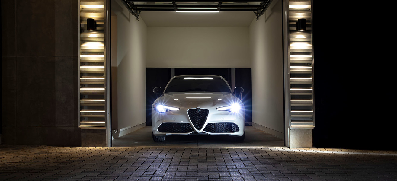 A front view of a white 2021 Alfa Romeo Giulia with LED headlights on parked in the garage at night