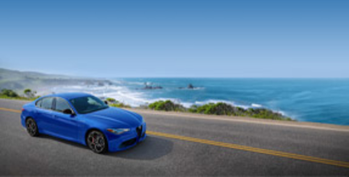 Side view of a blue Alfa Romeo Giulia, on a road near the sea.