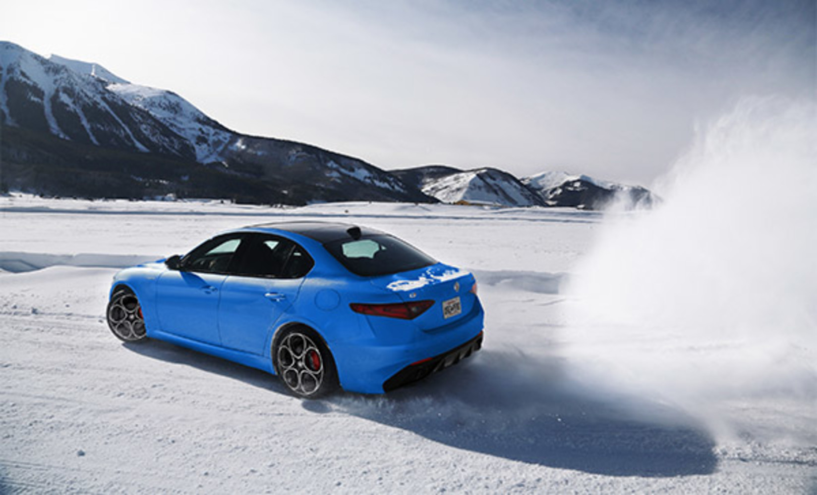Side view of a blue Alfa Romeo Giulia, driving on a snowy road in the mountains.