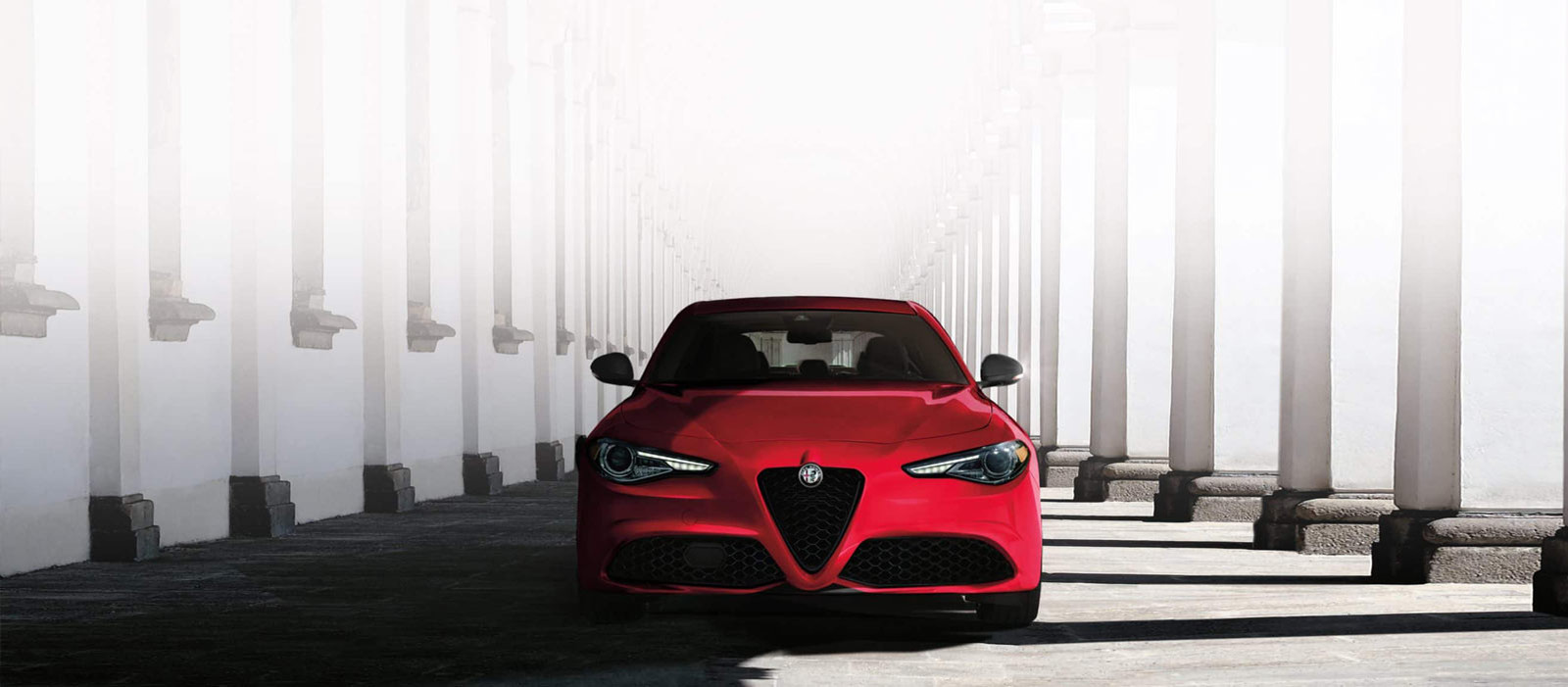 Vue de face d'une Alfa Romeo Giulia 2022 rouge roulant sur une route.