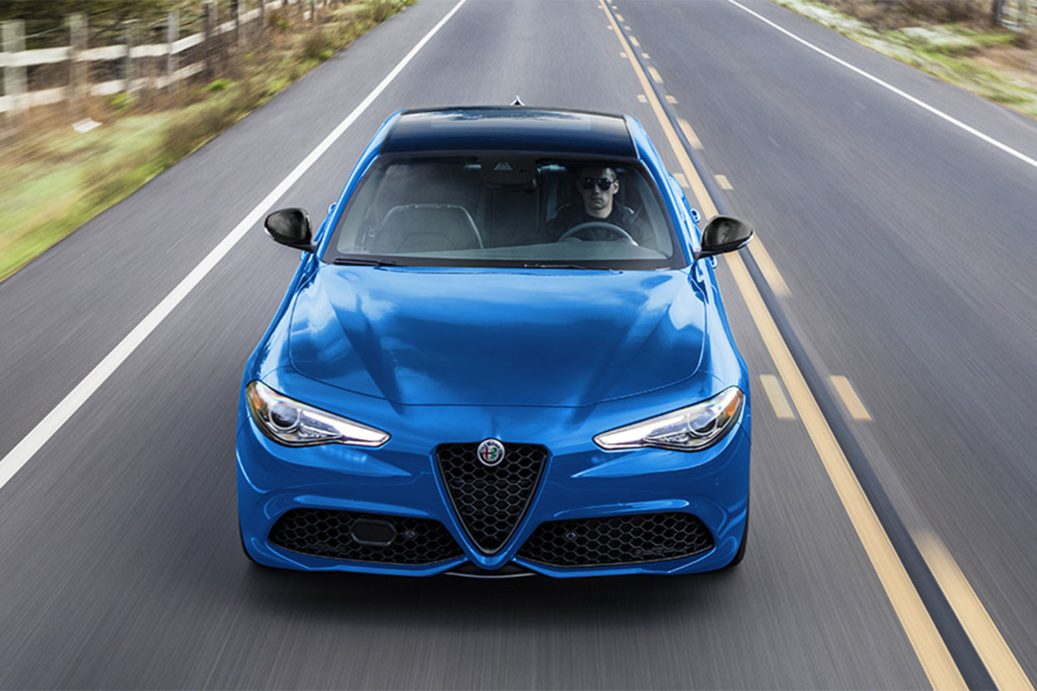 Front view of a blue 2023 Alfa Romeo Giulia driving on an open road.