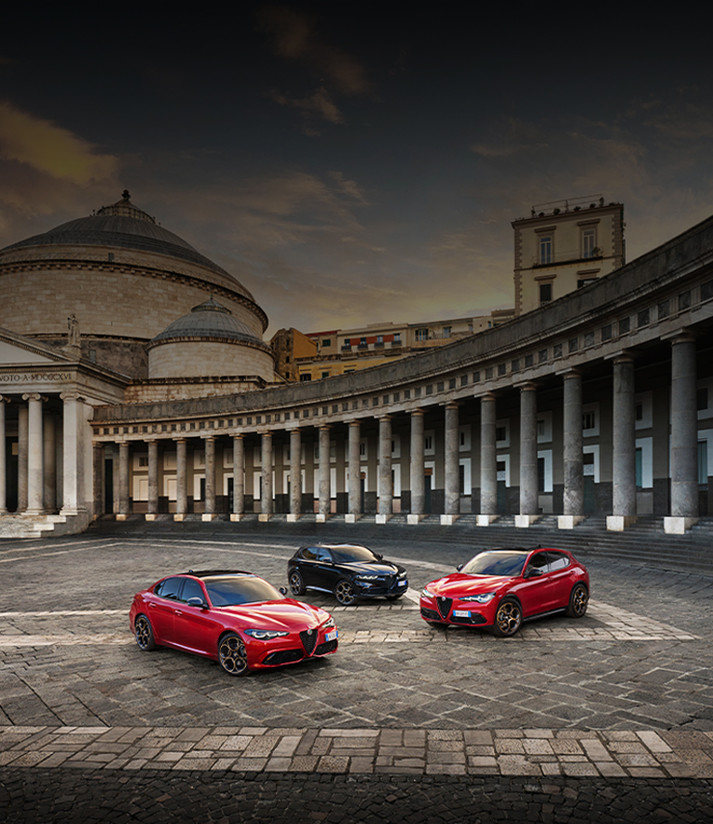 Trois véhicules Alfa Romeo 2025 sont garés sur une zone pavée devant un grand bâtiment. De gauche à droite : une Alfa Romeo Giulia rouge, une Alfa Romeo Tonale noire et une Alfa Romeo Stelvio rouge.