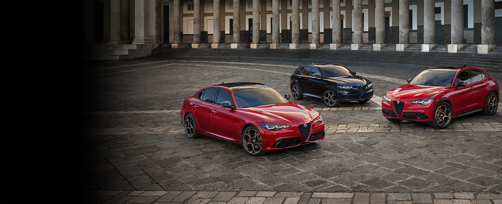 Trois véhicules Alfa Romeo 2025 sont garés sur une zone pavée devant un grand bâtiment. De gauche à droite : une Alfa Romeo Giulia rouge, une Alfa Romeo Tonale noire et une Alfa Romeo Stelvio rouge.