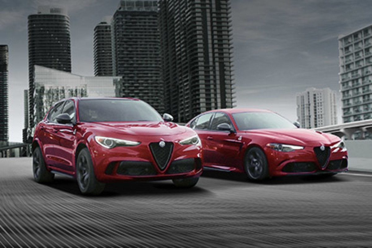 Une Alfa Romeo Stelvio rouge et une Alfa Romeo Giulia rouge garées sur une route pavée avec des gratte-ciel en arrière-plan.