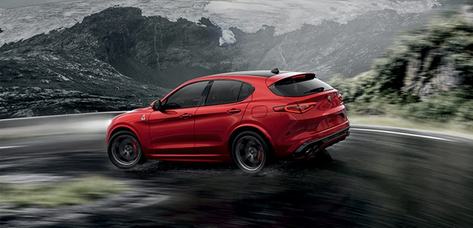 Vue arrière de l’Alfa Romeo Stelvio Quadrifoglio 2019, illustré en rouge, roulant sur une route mouillée dans les montagnes