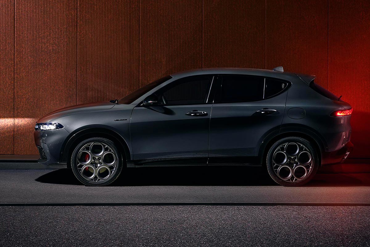 Élégant VUS électrique Alfa Romeo 2025 gris garé devant un mur couleur cuivre et branché pour la recharge.