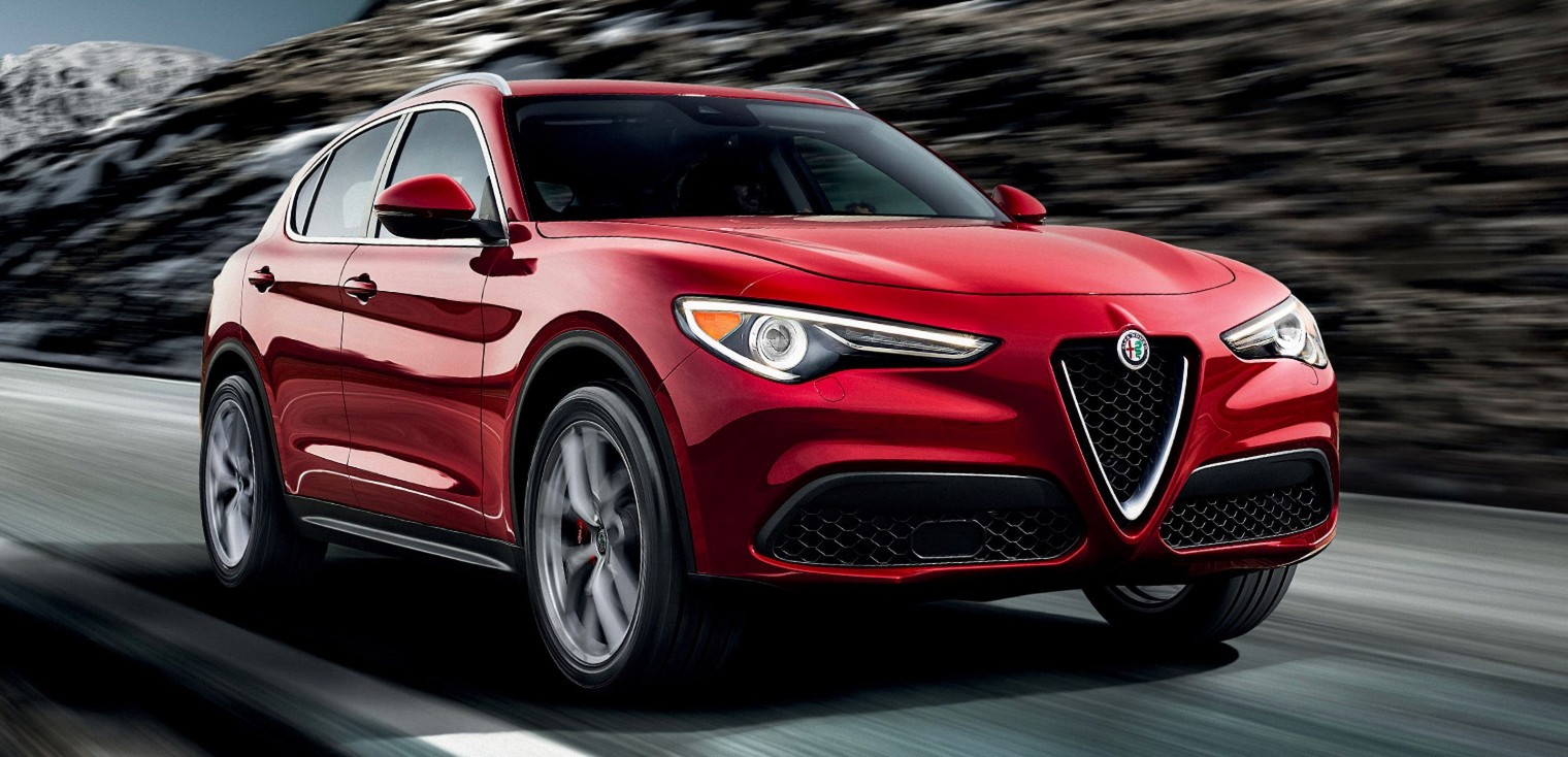 Vue de face de l’Alfa Romeo Stelvio 2019, illustré en rouge, roulant sur une route dans les montagnes