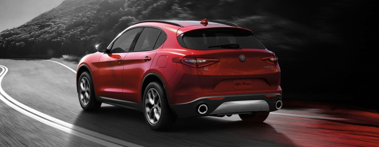 Rear view of the red 2019 Alfa Romeo driving down a road in the mountains