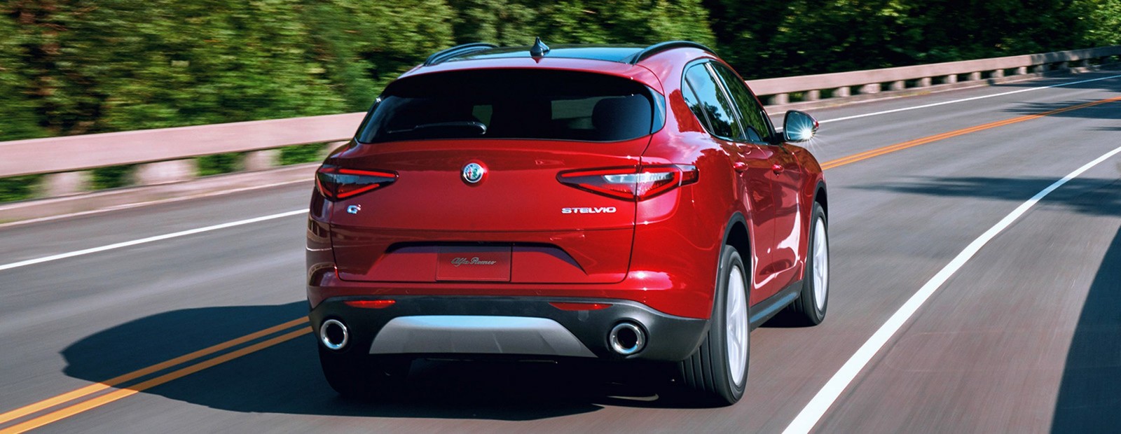 Rear view of the red 2019 Alfa Romeo Stelvio driving down a country road