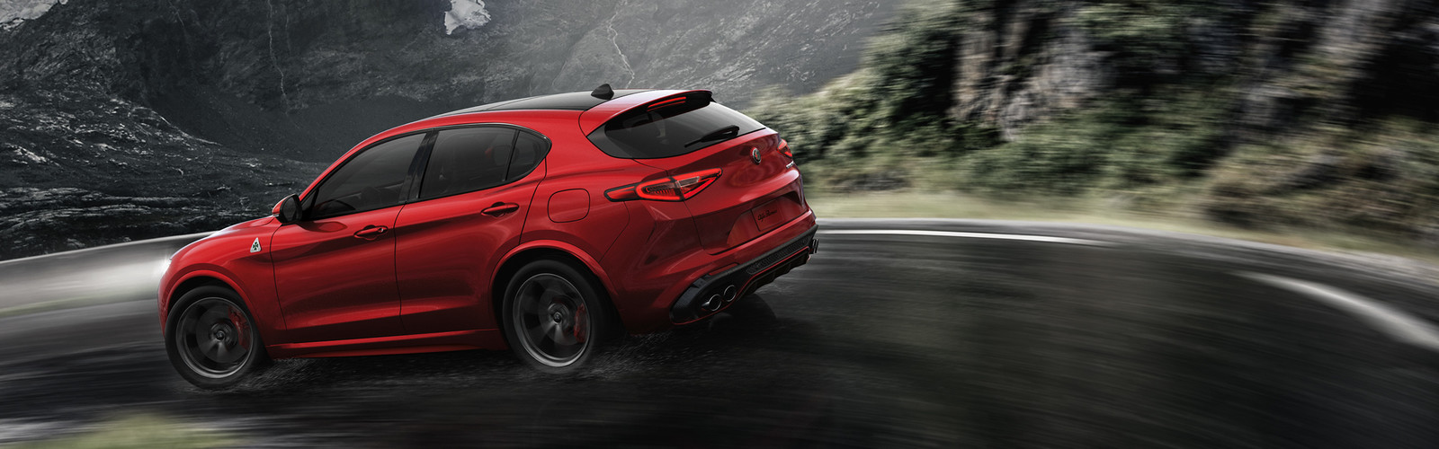 Rear view of the red 2019 Alfa Romeo Stelvio driving down a mountain road
