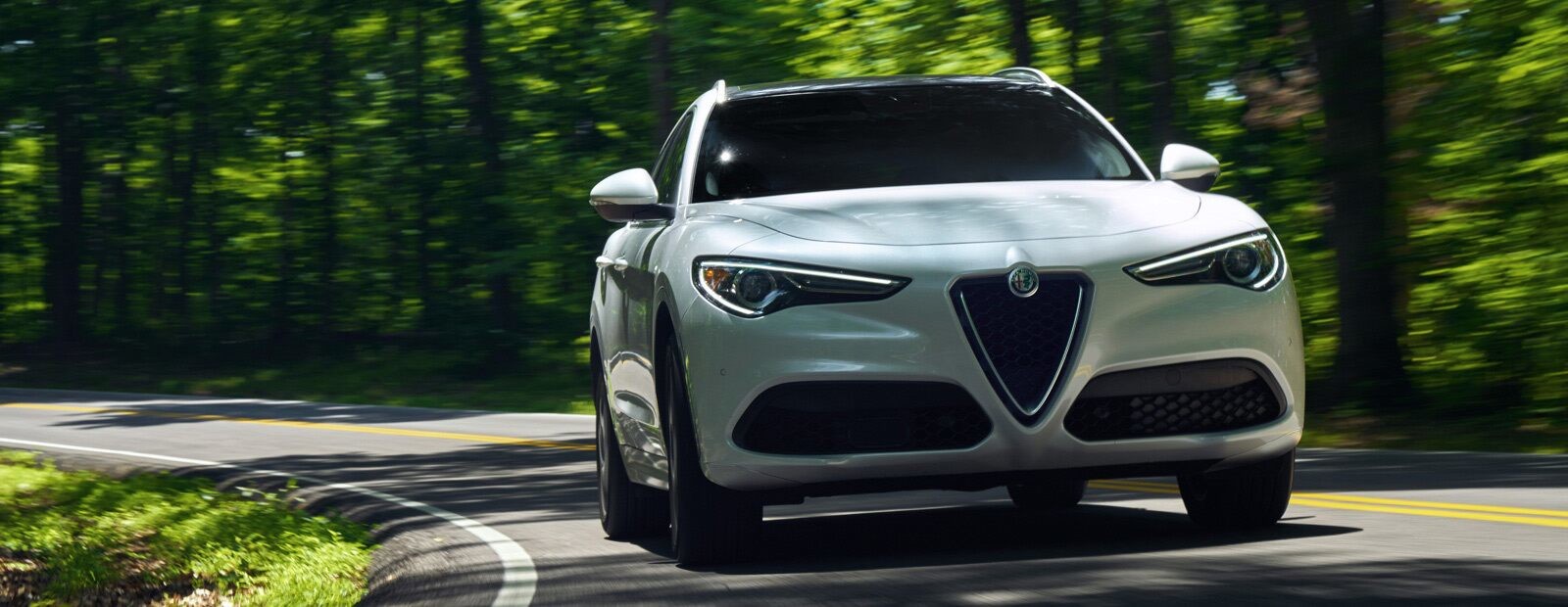 A front view of the 2020 Alfa Romeo Stelvio rounding a curve in the road.