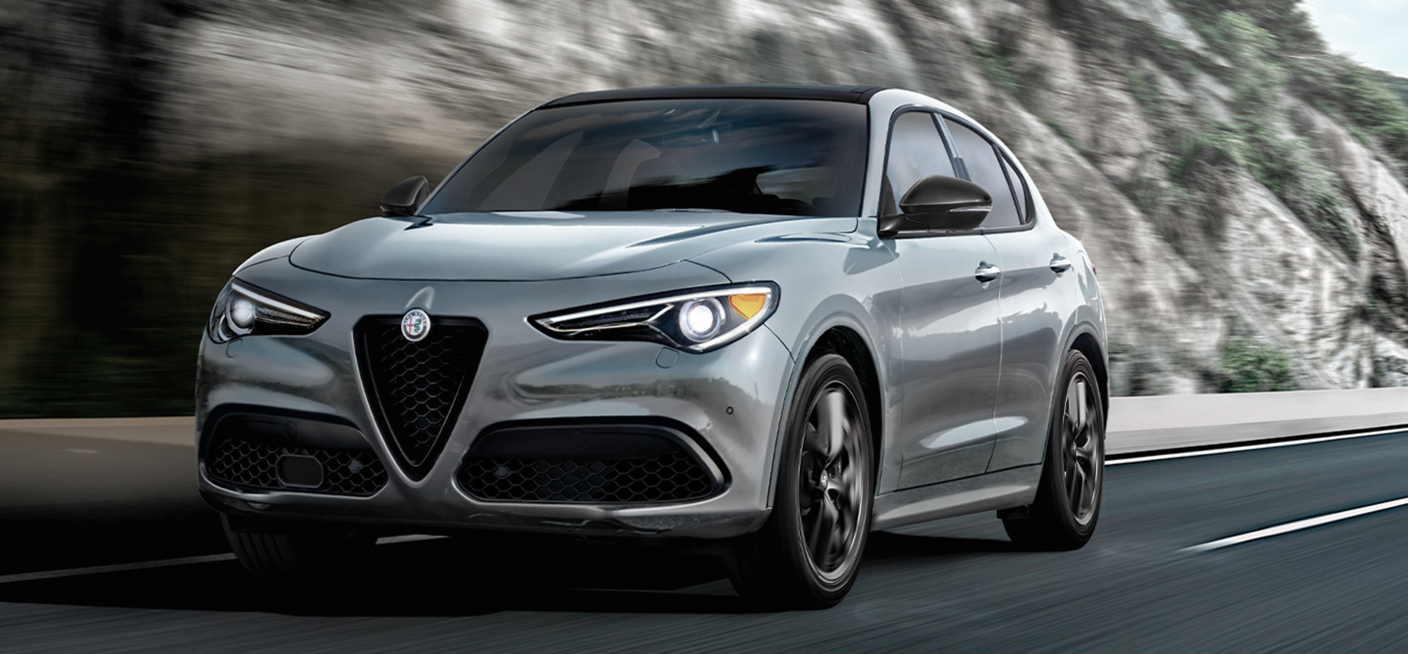 Front view of two 2021 Alfa Romeo Stelvio driving on a road with mountain behind