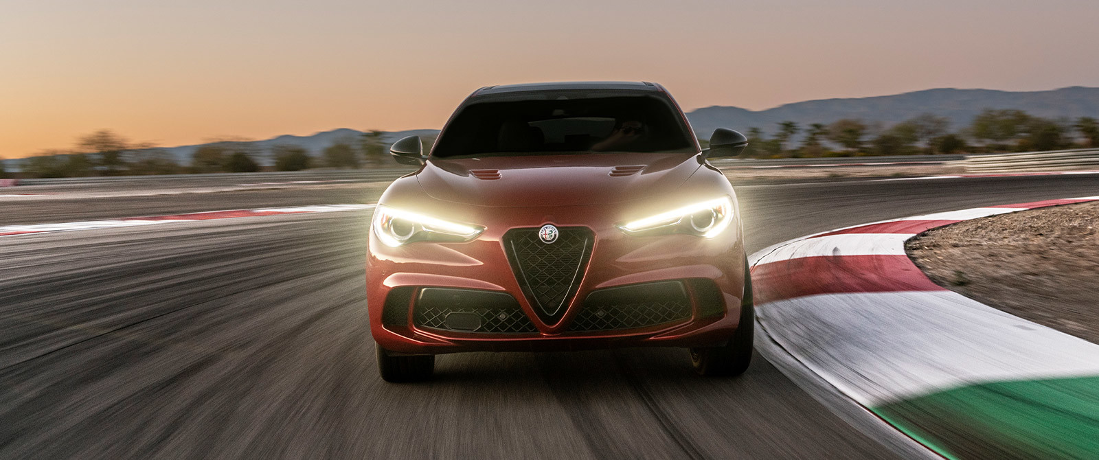 Vue frontale d’une Alfa Romeo Stelvio 2021 rouge illustrant les phares avants au DEL illuminant une piste de course.