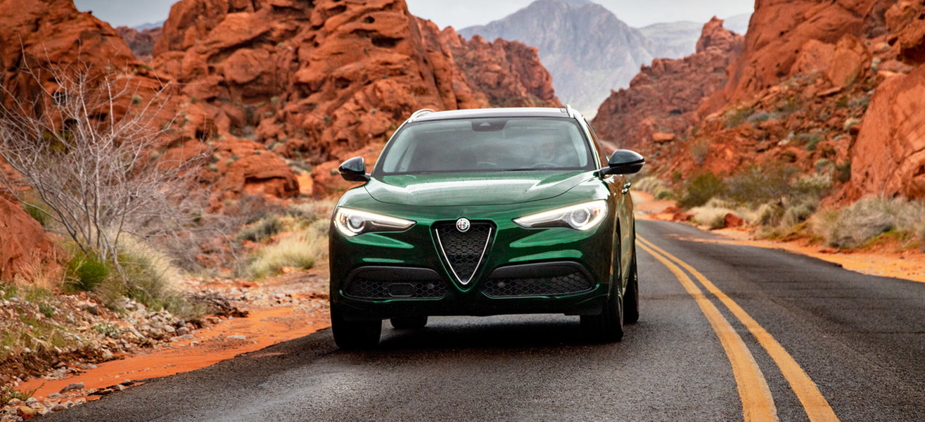 Green 2021 Alfa Romeo Stelvio driving through a quiet road surrounded by rocky mountains