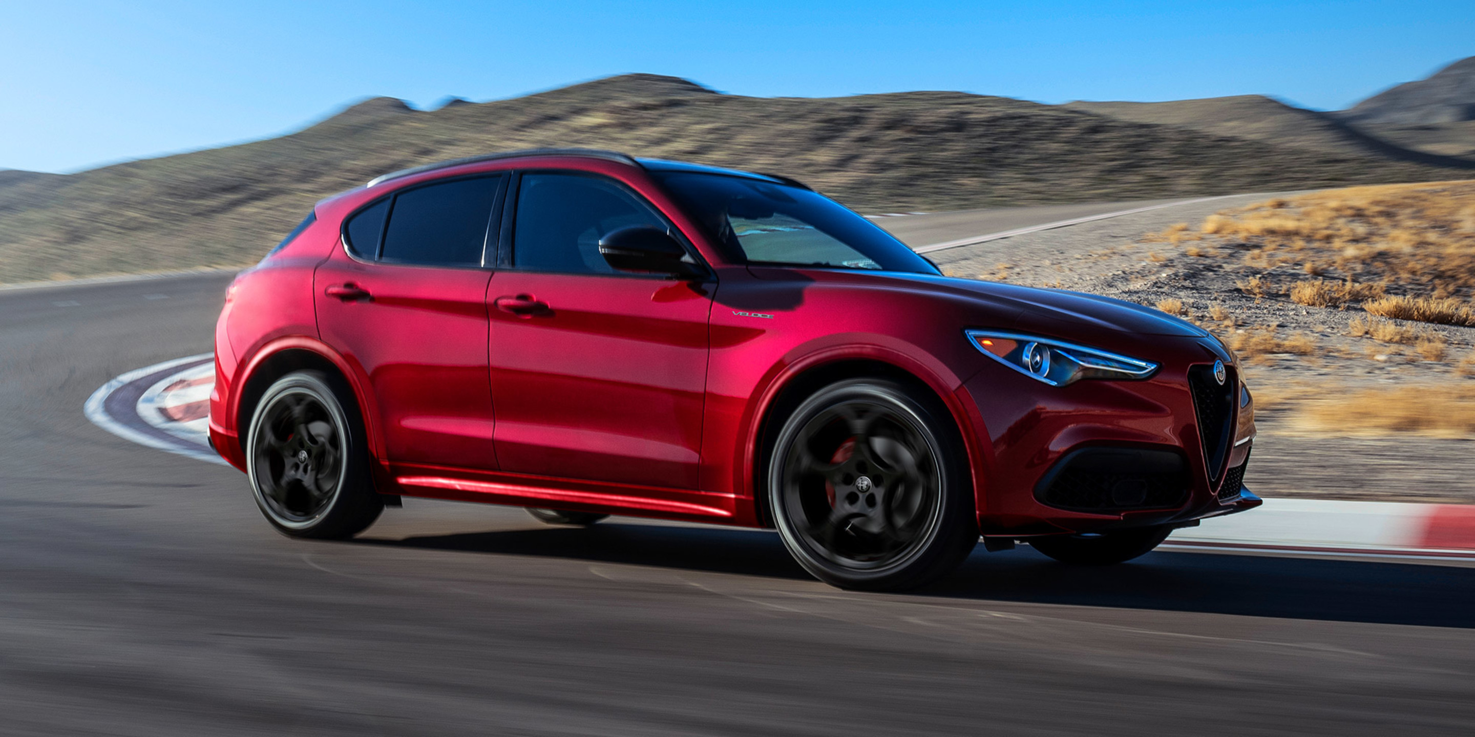 A red 2022 Alfa Romeo Stelvio driving in action on a backcountry road on a sunny day
