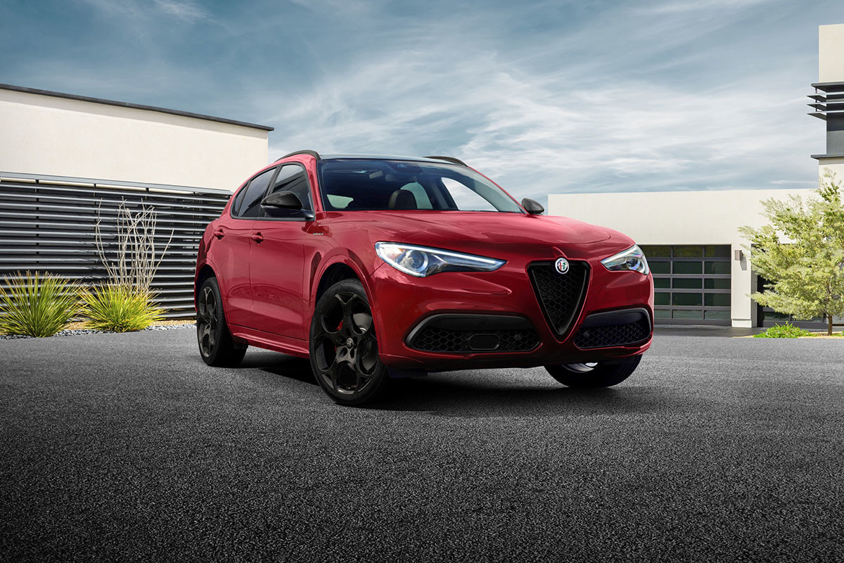 Vue latérale d’un Alfa Romeo Stelvio 2023 rouge stationné à l’extérieur d’un immeuble beige.
