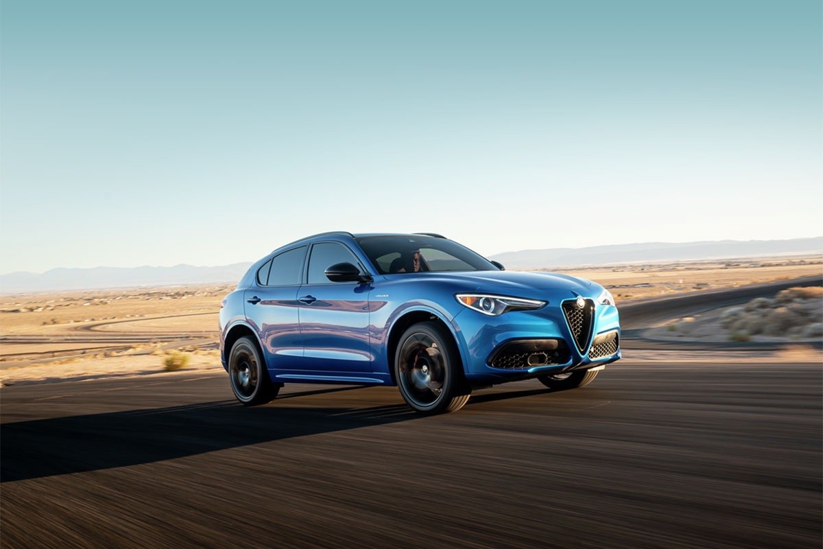 Vue d’un Alfa Romeo Stelvio 2023 bleu roulant sur une route pavée avec un désert en arrière-plan.