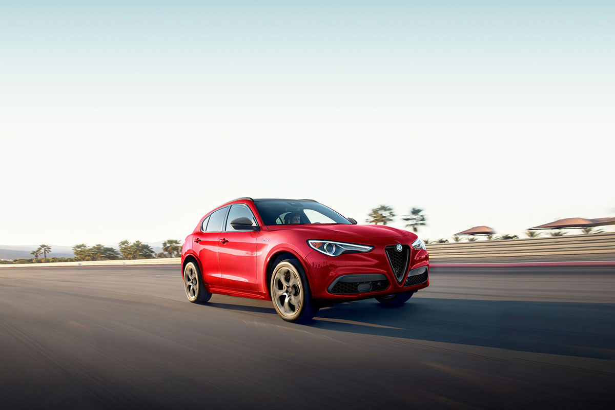 Vue en angle d'une Alfa Romeo Stelvio 2023 rouge roulant sur une route avec des arbres en arrière-plan.