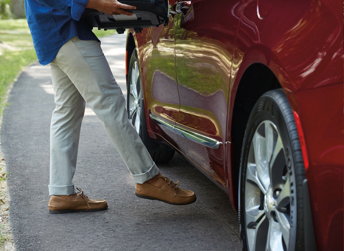 Man holding a car booster seat and using the hands-free door mechanism to open the side door of a red 2020 Chrysler Pacifica.