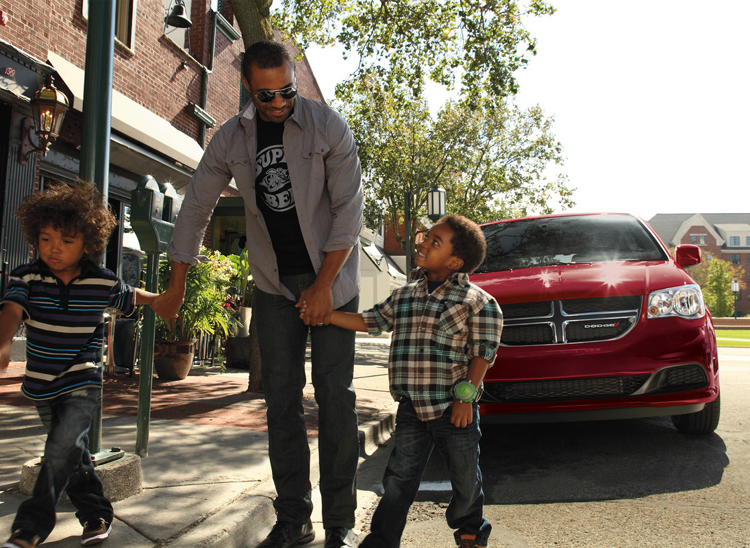 A red 2020 Dodge Grand Caravan parked on a street while two children and a man walk in front of it