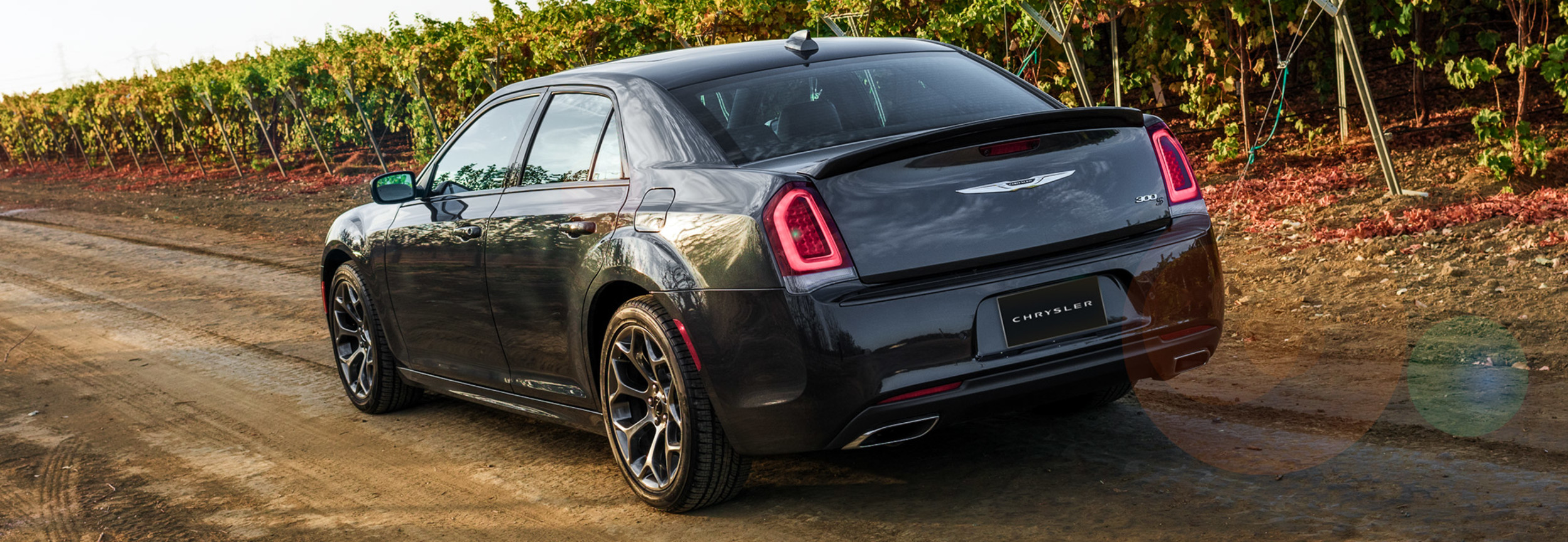 Chrysler 300 2020 grise roulant sur un chemin de terre entouré de vignobles.