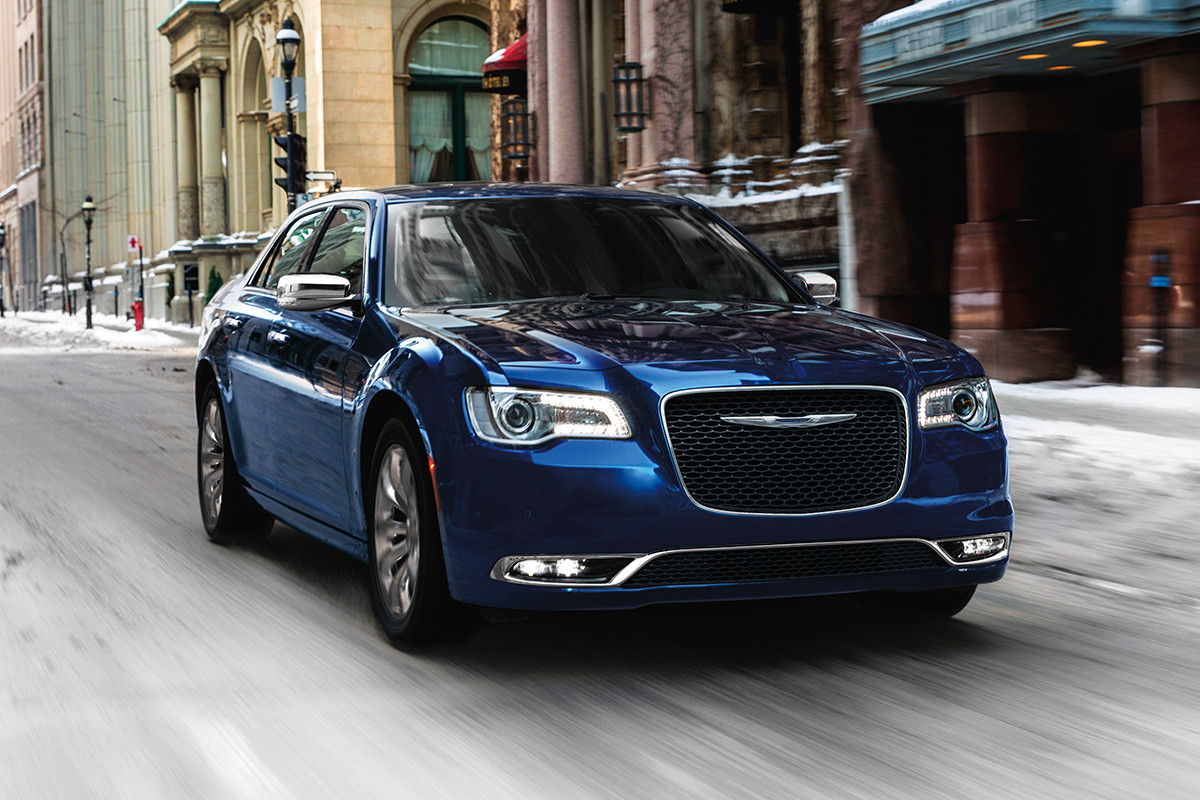 The blue 2020 Chrysler 300 driving through buildings on a road in a city