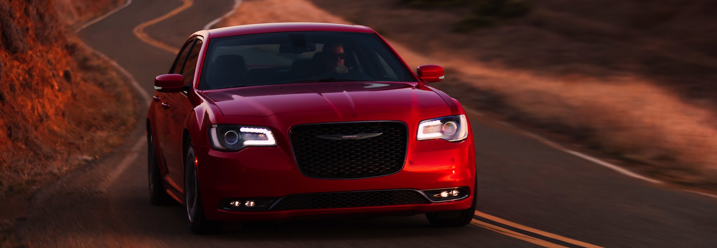 A front view of a Velvet Red Pearl 2021 Chrysler 300 on a desert road at sunset.