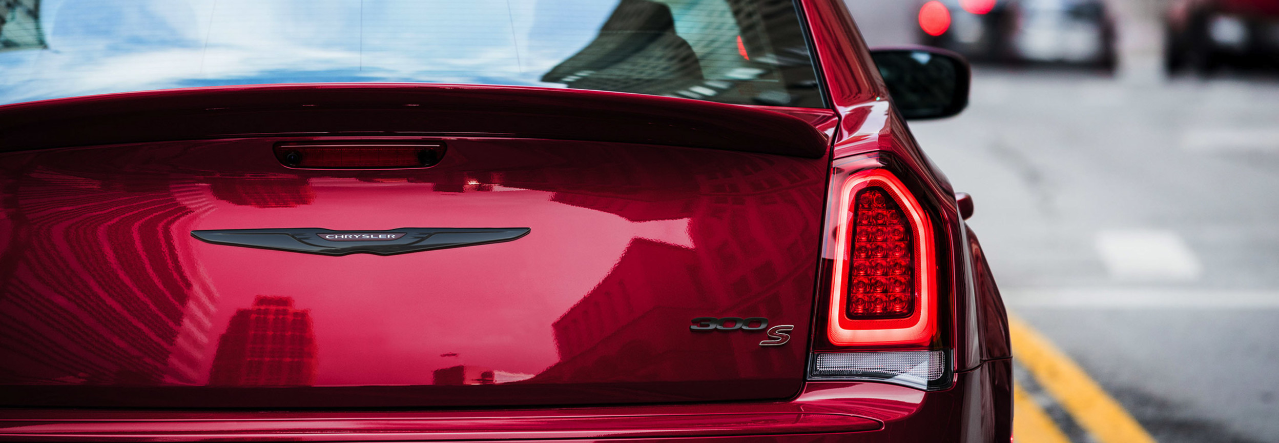 Vue arrière en gros plan d’une Chrysler 300S 2021 à couche nacrée rouge velours dans une rue de la ville.