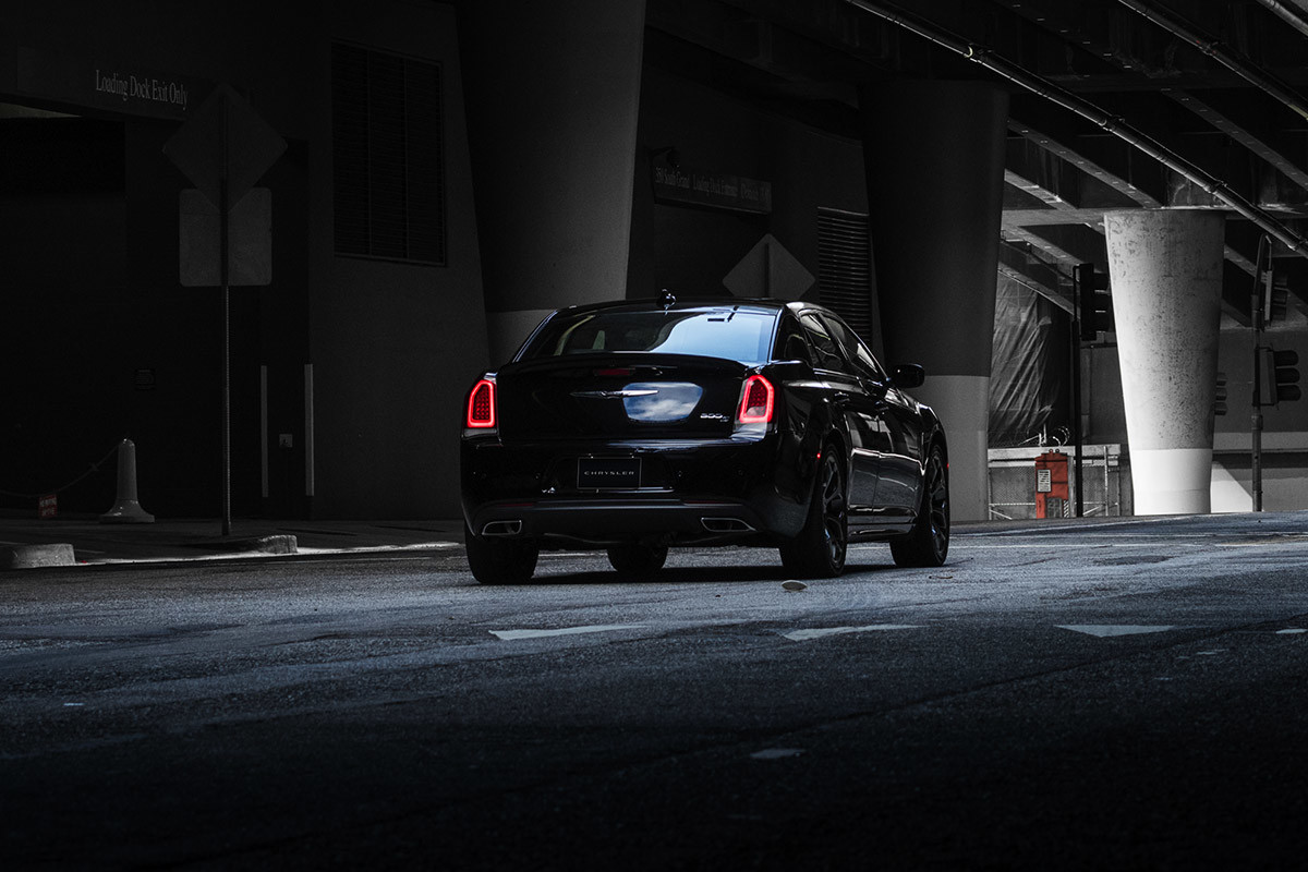 A rear view of a Gloss Black 2021 Chrysler 300 parked next to a building.