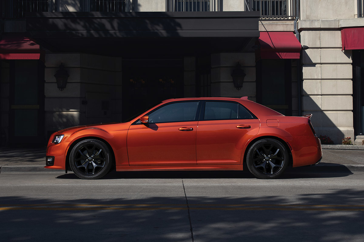 Vue latérale d’une Chrysler 300 2021 rouge canyon, garée devant l’entrée d’un immeuble en copropriété.