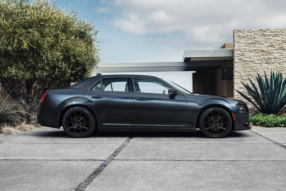 Vue latérale d’une Chrysler 300 2021 bleu glacial à roues noir bruit, garée devant un élégant pavillon.