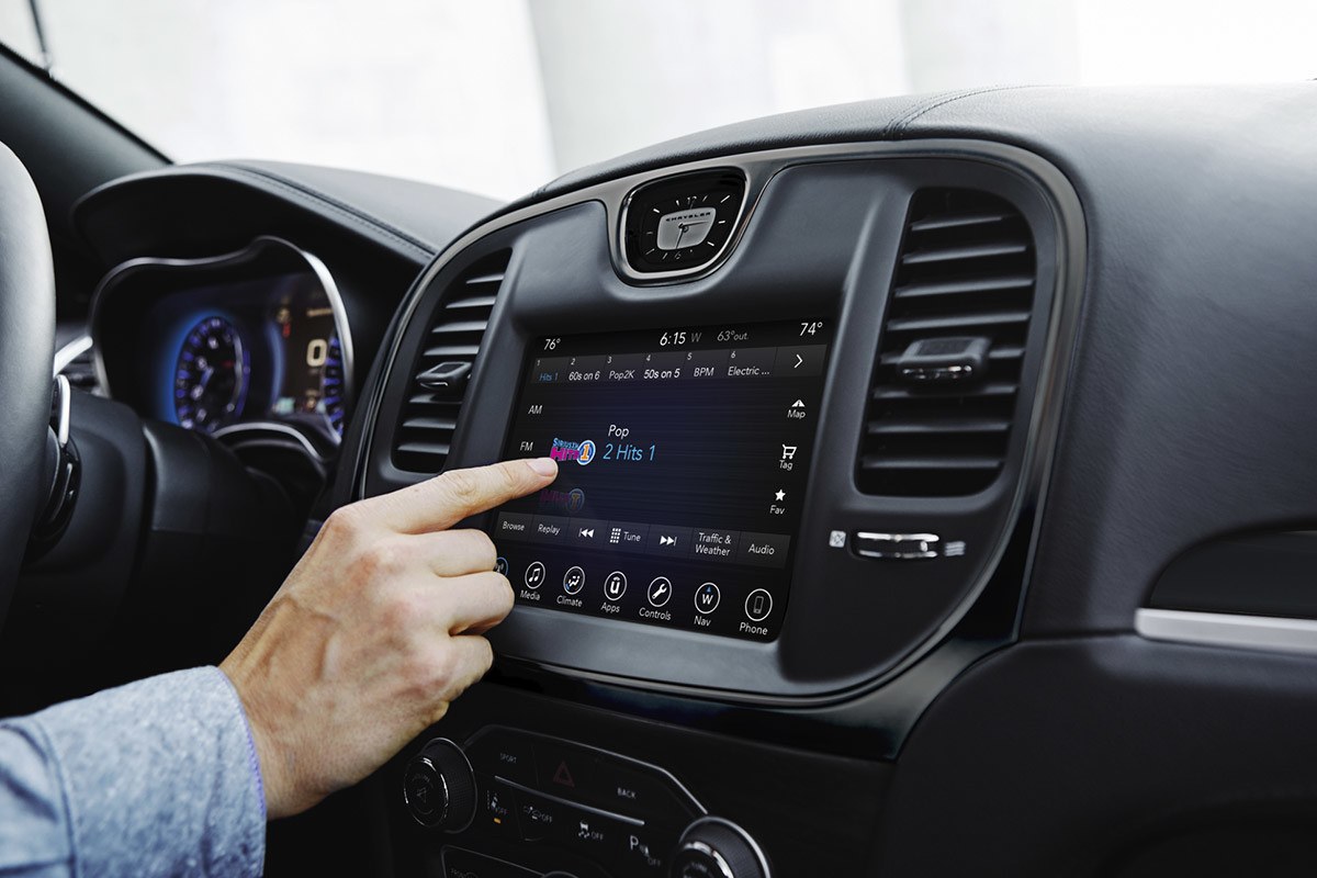 Gros plan de la main d’un conducteur sélectionnant de la musique au moyen du centre multimédia Uconnect à écran tactile de 8,4 po de la Chrysler 300 2021.