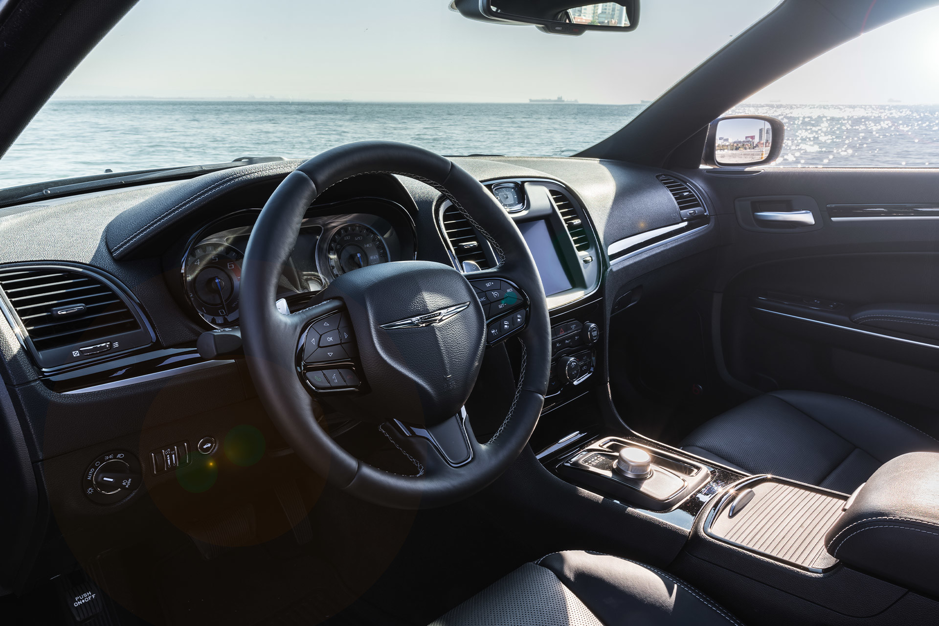 Gros plan du volant gainé de cuir d’une Chrysler 300S 2021, garée au bord d’un lac étincelant.