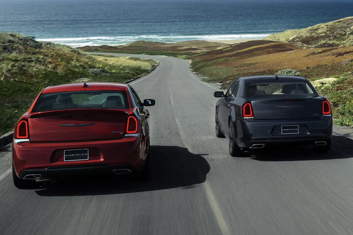 A red and grey Chrysler 300 driving down an open road showing the blind-spot monitoring feature.