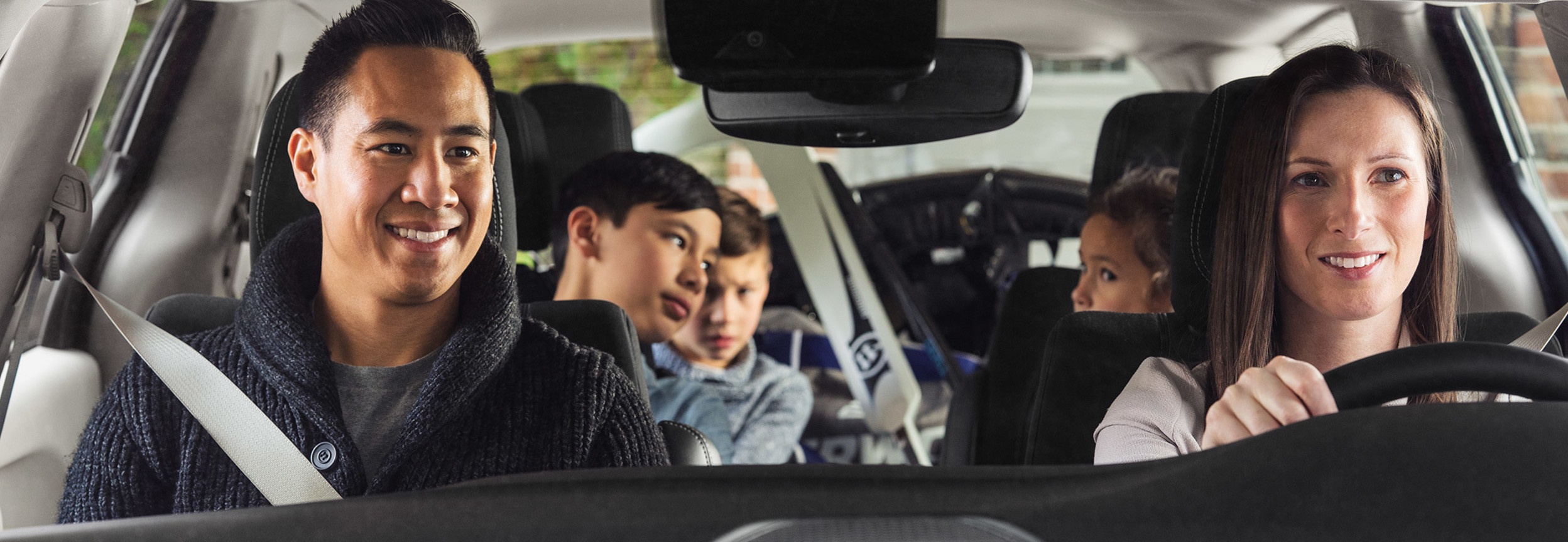 A close-up front view of a 2021 Chrysler Grand Caravan being driven by a woman with her family in the passenger seats.