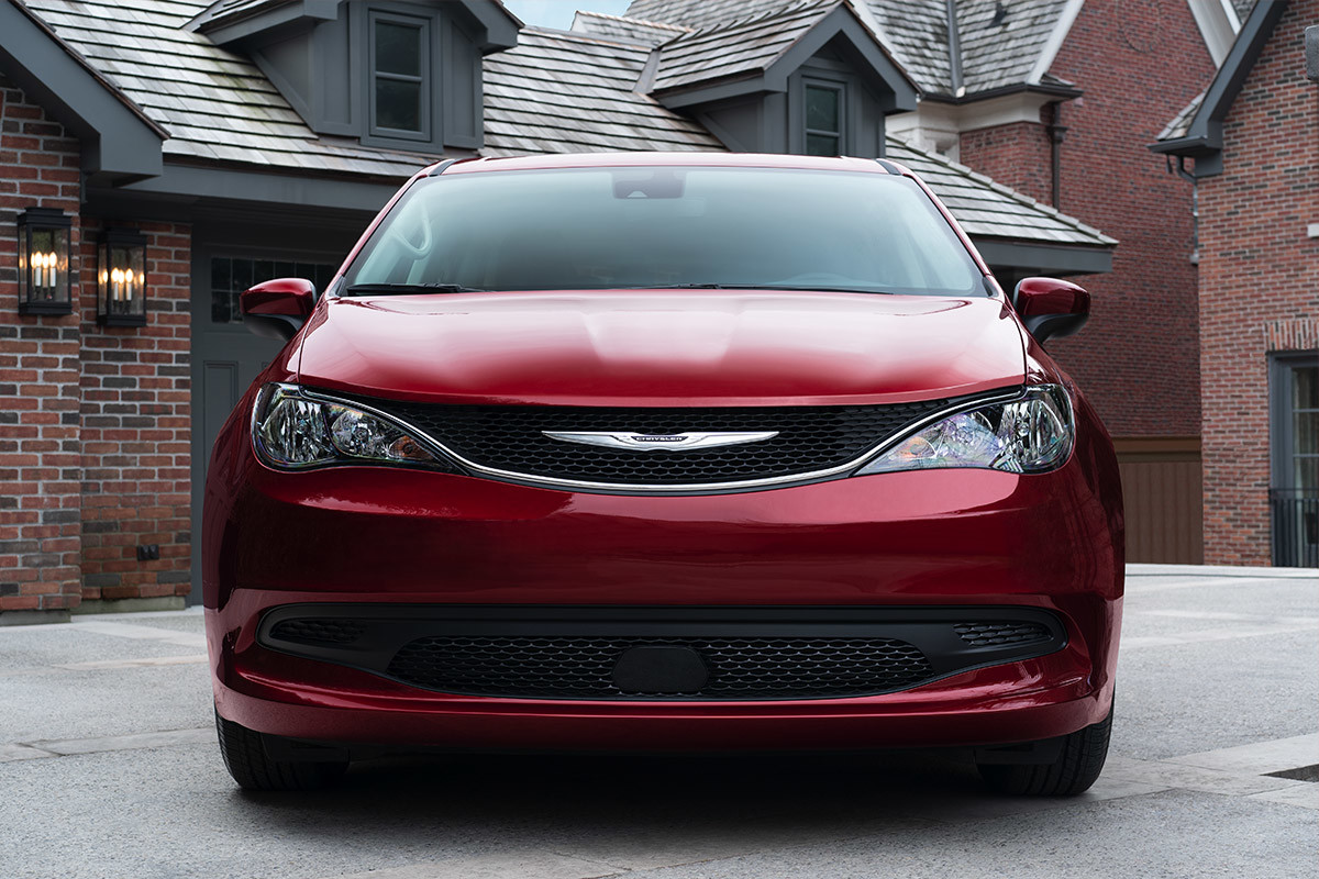 A front view of the contoured exterior of a Velvet Red Pearl 2021 Chrysler Grand Caravan parked on a driveway in front of a red-bricked home.