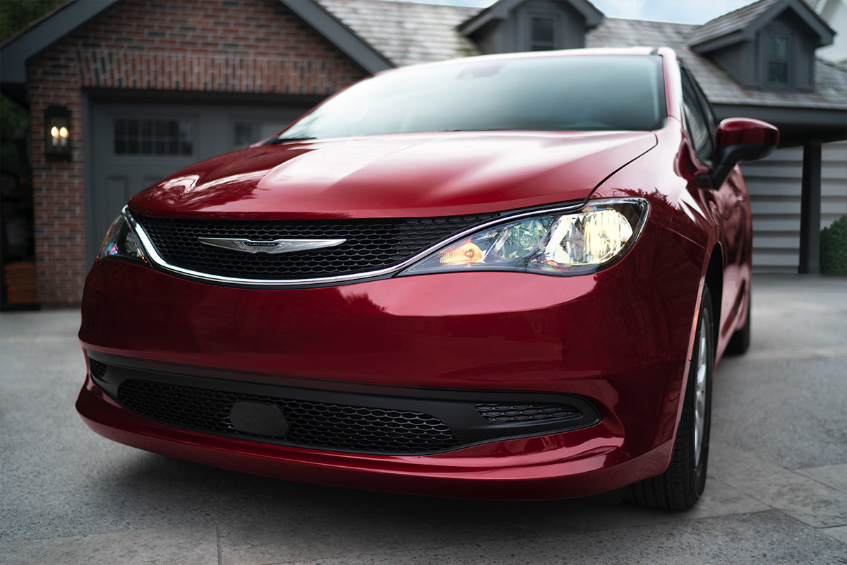 A front view of a Velvet Red Pearl 2021 Chrysler Grand Caravan with standard halogen headlamps parked on the driveway of a bungalow.